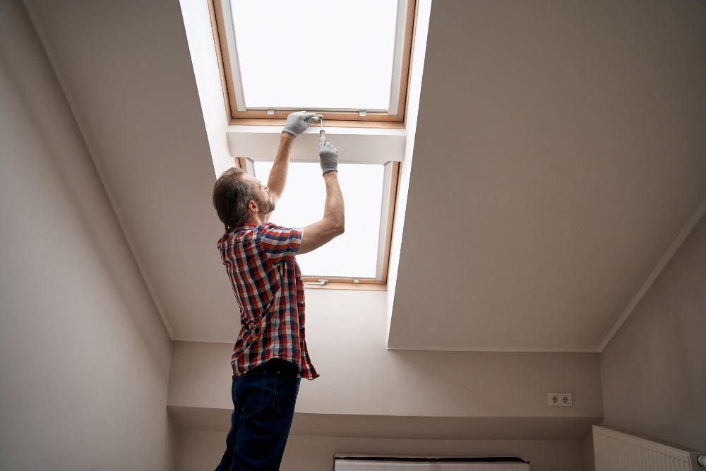Young caucasian repairman screwing handle on skylight window standing sideways with raised hands.